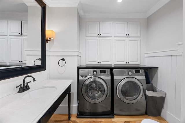 washroom featuring washer and clothes dryer, cabinet space, wainscoting, crown molding, and a decorative wall