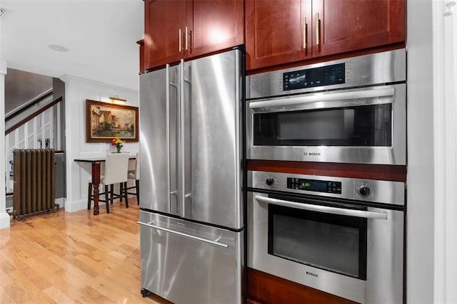 kitchen with stainless steel appliances, radiator heating unit, light wood-style flooring, and dark brown cabinets