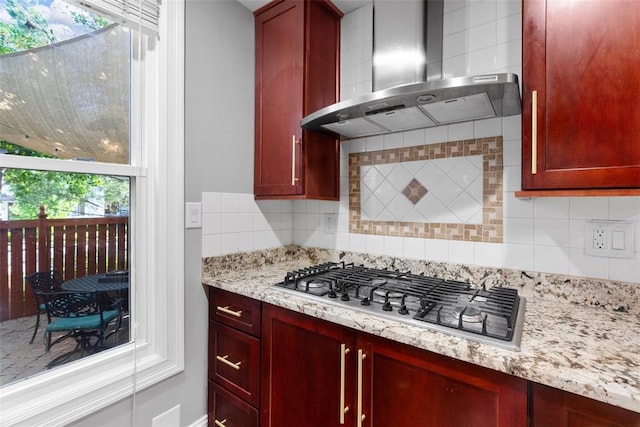 kitchen featuring wall chimney exhaust hood, stainless steel gas cooktop, reddish brown cabinets, and backsplash