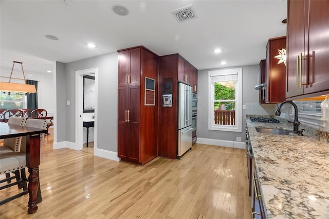 kitchen with a sink, reddish brown cabinets, appliances with stainless steel finishes, light wood-style floors, and light stone counters