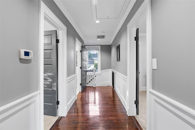 corridor featuring attic access, a decorative wall, ornamental molding, wood-type flooring, and a wainscoted wall