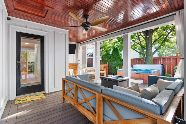 wooden terrace with a hot tub, a ceiling fan, an outdoor living space with a fire pit, and fence
