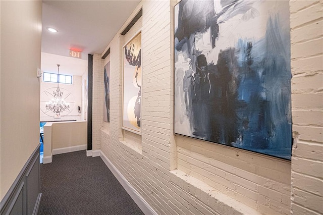 hall featuring dark carpet, baseboards, and a chandelier