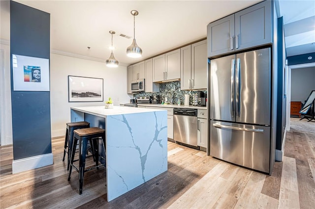 kitchen featuring appliances with stainless steel finishes, a kitchen island, light wood finished floors, decorative backsplash, and ornamental molding
