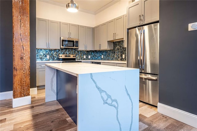 kitchen featuring stainless steel appliances, ornamental molding, light wood-style floors, light stone counters, and a center island