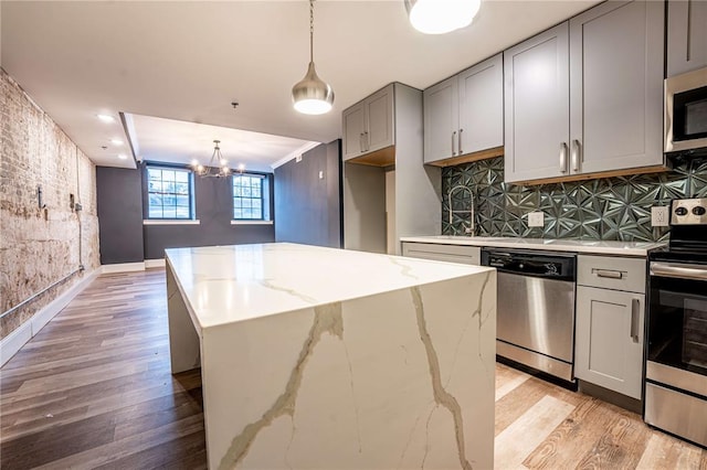 kitchen featuring stainless steel appliances, gray cabinets, light wood-type flooring, a chandelier, and decorative backsplash