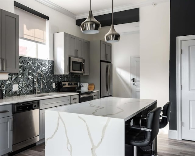 kitchen with appliances with stainless steel finishes, gray cabinets, a sink, a kitchen island, and decorative backsplash