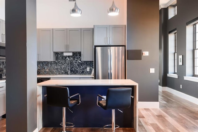 kitchen with freestanding refrigerator, light countertops, a kitchen breakfast bar, decorative backsplash, and light wood-type flooring