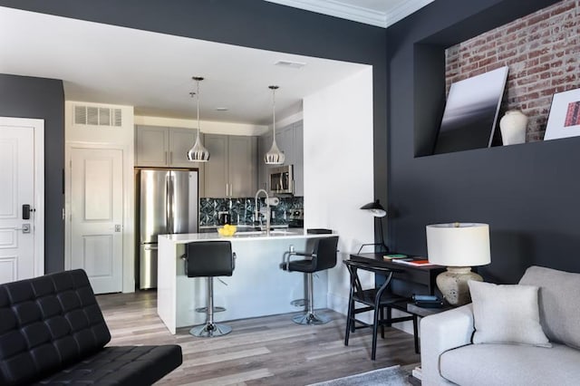 kitchen with stainless steel appliances, open floor plan, a kitchen bar, gray cabinets, and crown molding
