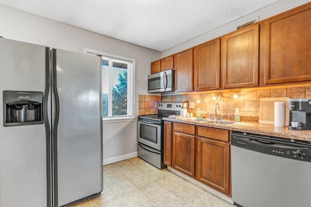 1843 Gascony Parc Dr Unit 1843, Lake St Louis, MO 63367 - kitchen featuring appliances with stainless steel finishes, tasteful backsplash, a sink, brown cabinetry, and a textured ceiling