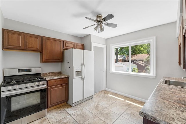 8908 Apache Ln, Overland, MO 63114 - kitchen featuring stainless steel gas stove, white fridge with ice dispenser, a sink, baseboards, and brown cabinets
