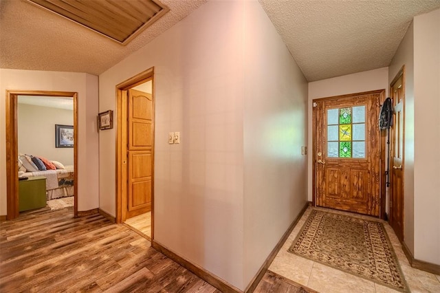 doorway to outside featuring a textured ceiling, light wood finished floors, and baseboards