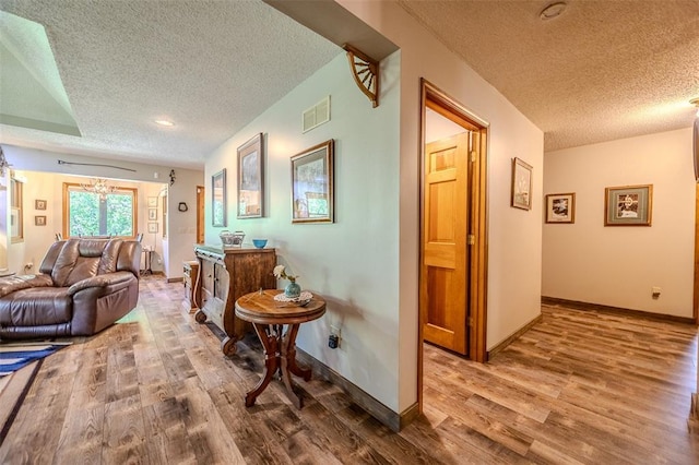 corridor with a textured ceiling, wood finished floors, and baseboards