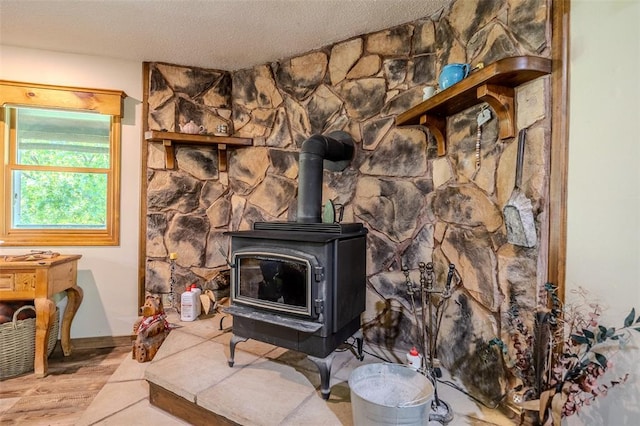 detailed view of a wood stove, wood finished floors, a textured ceiling, and baseboards