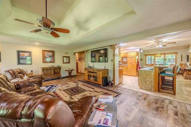 living area featuring a ceiling fan, light wood finished floors, and a raised ceiling