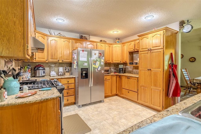 kitchen with stainless steel appliances, under cabinet range hood, a textured ceiling, tasteful backsplash, and light stone countertops