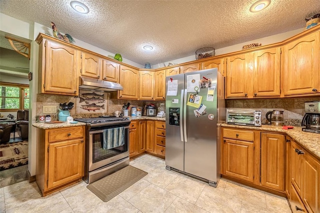 kitchen with appliances with stainless steel finishes, under cabinet range hood, decorative backsplash, light stone countertops, and a textured ceiling