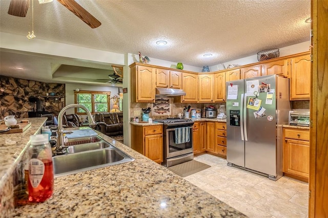 kitchen featuring a ceiling fan, stainless steel appliances, a sink, a wood stove, and under cabinet range hood