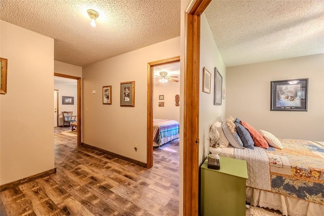 hall featuring wood finished floors, a textured ceiling, and baseboards