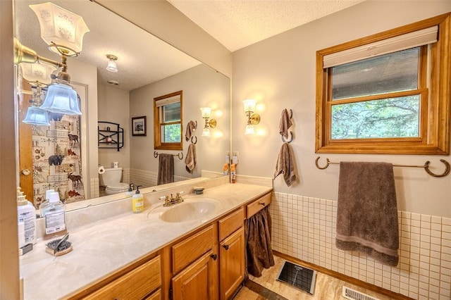 bathroom featuring a wainscoted wall, plenty of natural light, toilet, vanity, and a textured ceiling