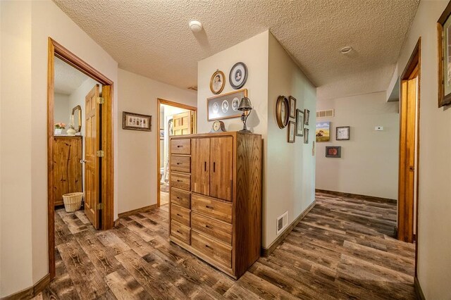 hallway with dark wood-style flooring, a textured ceiling, and baseboards