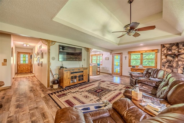 living area featuring wood finished floors, a tray ceiling, ceiling fan, and baseboards