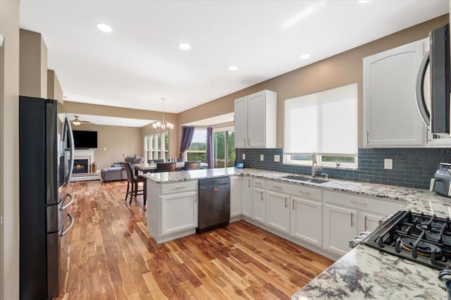 5 The Crossings Ct, Ofallon, MO 63366 - kitchen featuring appliances with stainless steel finishes, a sink, open floor plan, white cabinets, and a warm lit fireplace