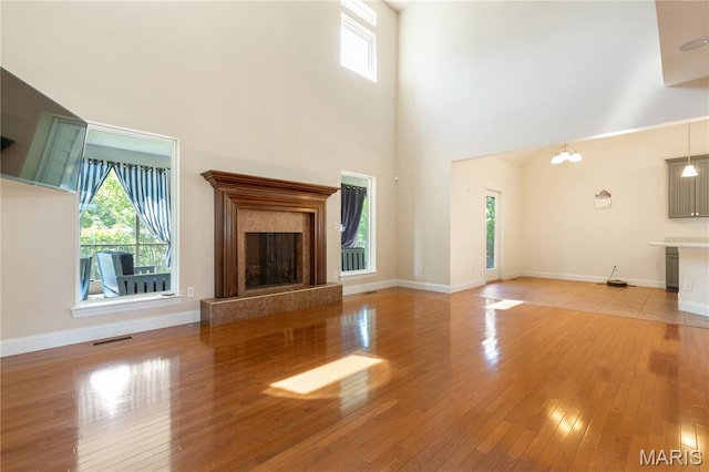 106 Tuscany Trace Dr, Saint Charles, MO 63303 - unfurnished living room with a high end fireplace, light wood-style floors, a towering ceiling, baseboards, and a chandelier