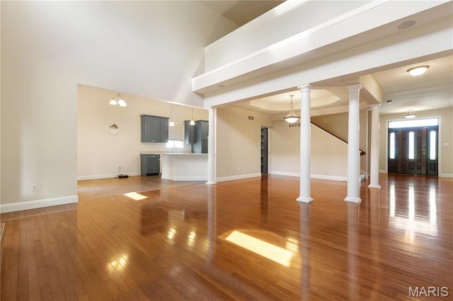106 Tuscany Trace Dr, Saint Charles, MO 63303 - unfurnished living room with light wood-style floors, decorative columns, baseboards, and a towering ceiling