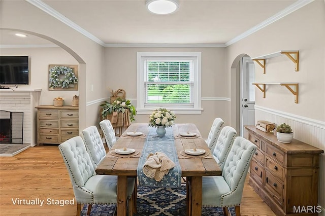 6446 Old Collinsville Rd, Ofallon, IL 62269 - dining space featuring arched walkways, light wood-style flooring, ornamental molding, a brick fireplace, and wainscoting
