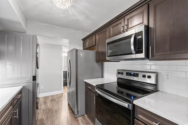 1491 Bobolink Pl, Brentwood, MO 63144 - kitchen with stainless steel appliances, dark brown cabinets, light wood-style floors, tasteful backsplash, and stacked washer and clothes dryer