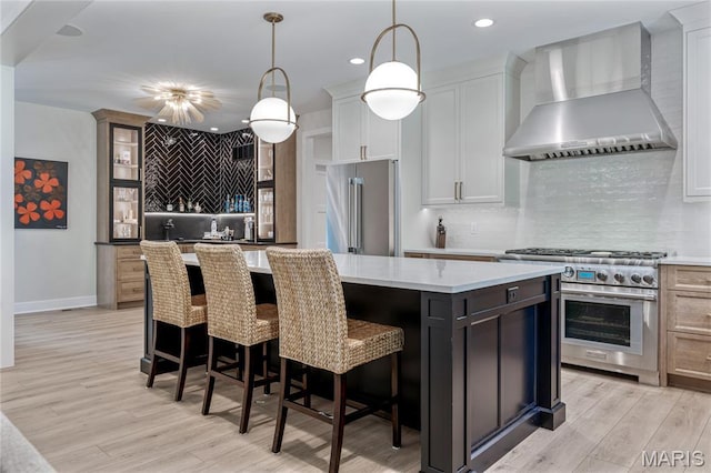 100 Enclave Terrace Ct, Weldon Spring, MO 63304 - kitchen featuring wall chimney range hood, high quality appliances, tasteful backsplash, a center island, and light wood finished floors