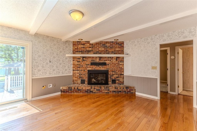 21509 Rockwell Dr, Lebanon, MO 65536 - unfurnished living room featuring wainscoting, hardwood / wood-style flooring, beam ceiling, wallpapered walls, and a textured ceiling