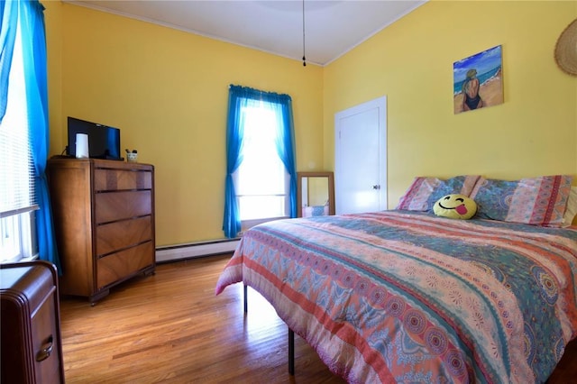 bedroom featuring a baseboard heating unit, wood finished floors, and ornamental molding