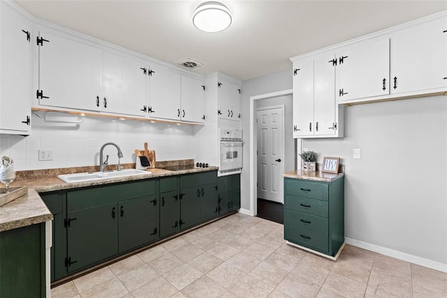 kitchen with a sink, oven, green cabinets, backsplash, and baseboards