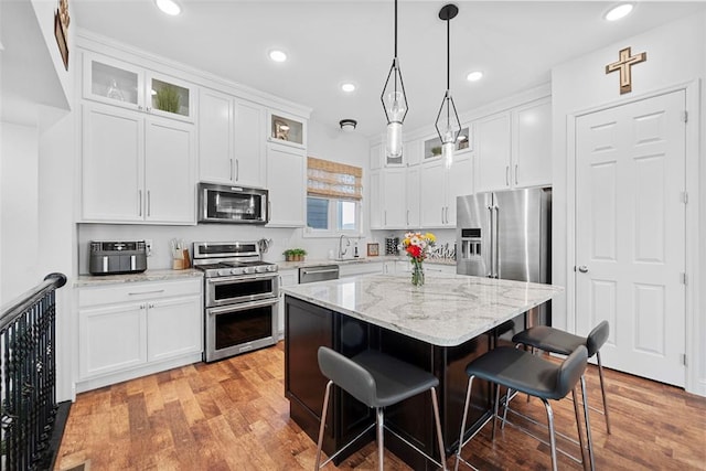1017 Kilderkin Way, Saint Charles, MO 63301 - kitchen featuring appliances with stainless steel finishes, a kitchen breakfast bar, glass insert cabinets, white cabinetry, and recessed lighting