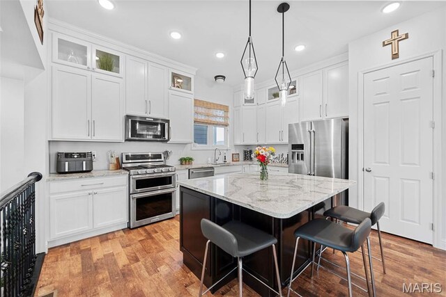 1017 Kilderkin Way, Saint Charles, MO 63301 - kitchen featuring appliances with stainless steel finishes, a kitchen breakfast bar, glass insert cabinets, white cabinetry, and recessed lighting
