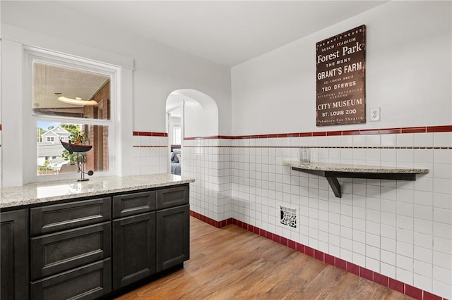6927 Lansdowne Ave, Saint Louis, MO 63109 - kitchen with tile walls, arched walkways, light stone counters, light wood-style flooring, and wainscoting