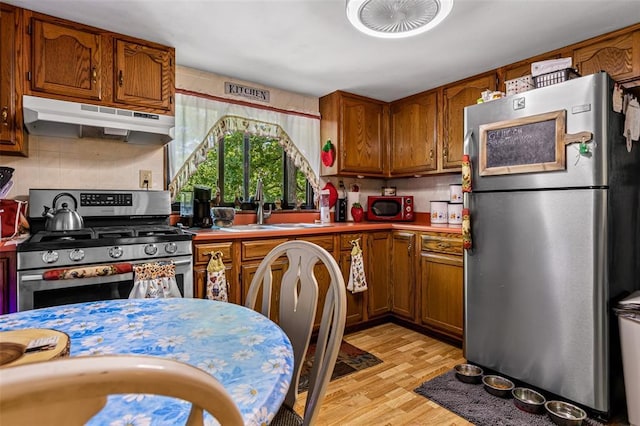 14135 Oak Dr, De Soto, MO 63020 - kitchen with appliances with stainless steel finishes, under cabinet range hood, brown cabinets, light wood-style flooring, and light countertops
