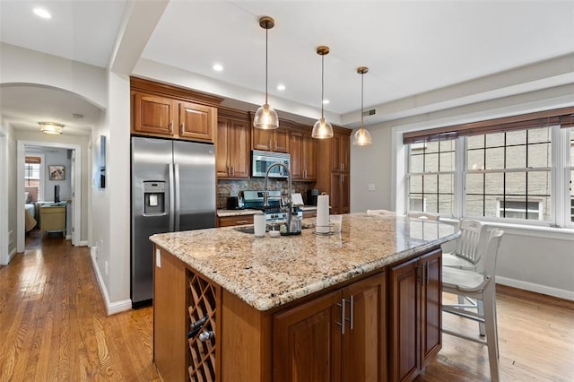 7520 Buckingham Dr Unit 1W, Saint Louis, MO 63105 - kitchen featuring appliances with stainless steel finishes, arched walkways, tasteful backsplash, light stone counters, and brown cabinets