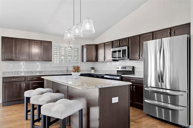 217 Arlington Dr, Moscow Mills, MO 63362 - kitchen featuring stainless steel appliances, vaulted ceiling, dark brown cabinetry, tasteful backsplash, and a center island