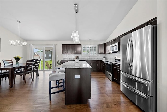 217 Arlington Dr, Moscow Mills, MO 63362 - kitchen featuring appliances with stainless steel finishes, vaulted ceiling, decorative backsplash, a center island, and dark brown cabinetry