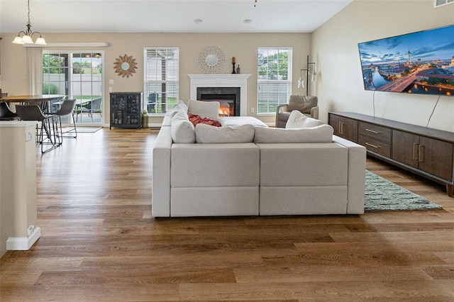 living room with plenty of natural light, a glass covered fireplace, wood finished floors, and a chandelier
