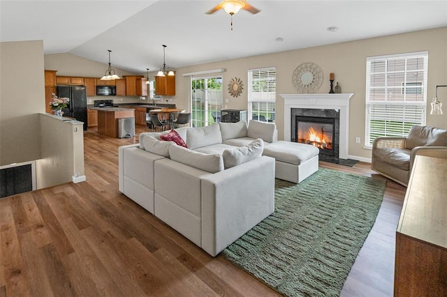 living area with wood finished floors, a ceiling fan, a fireplace, and lofted ceiling