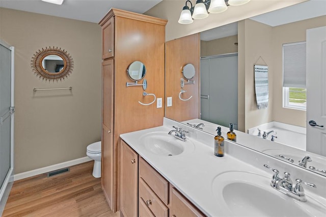 bathroom featuring wood finished floors, a stall shower, toilet, baseboards, and double vanity