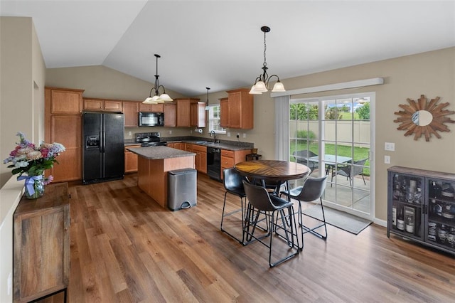 kitchen with black appliances, a sink, wood finished floors, a kitchen island, and lofted ceiling