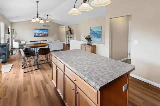 kitchen with wood finished floors, a center island, vaulted ceiling, and pendant lighting