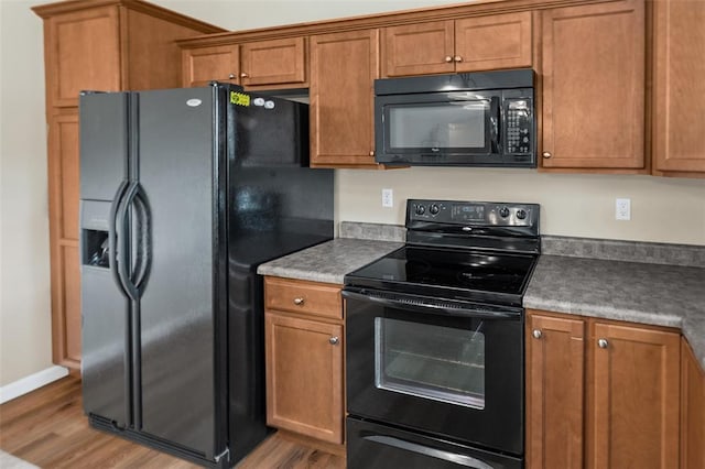 kitchen featuring black appliances, brown cabinets, wood finished floors, and baseboards