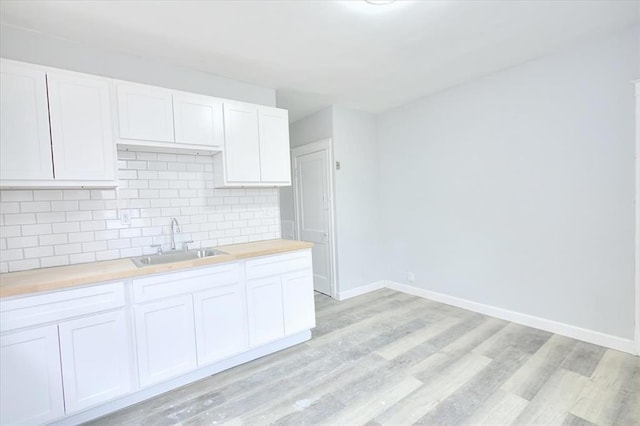 5027 S Broadway Ave Unit 1-4, Saint Louis, MO 63111 - kitchen featuring a sink, light wood-style floors, baseboards, decorative backsplash, and white cabinets