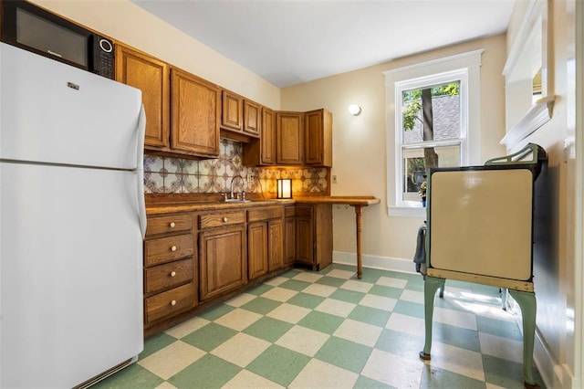 7511 Milan Ave, University City, MO 63130 - kitchen featuring freestanding refrigerator, light flooring, brown cabinets, decorative backsplash, and a sink